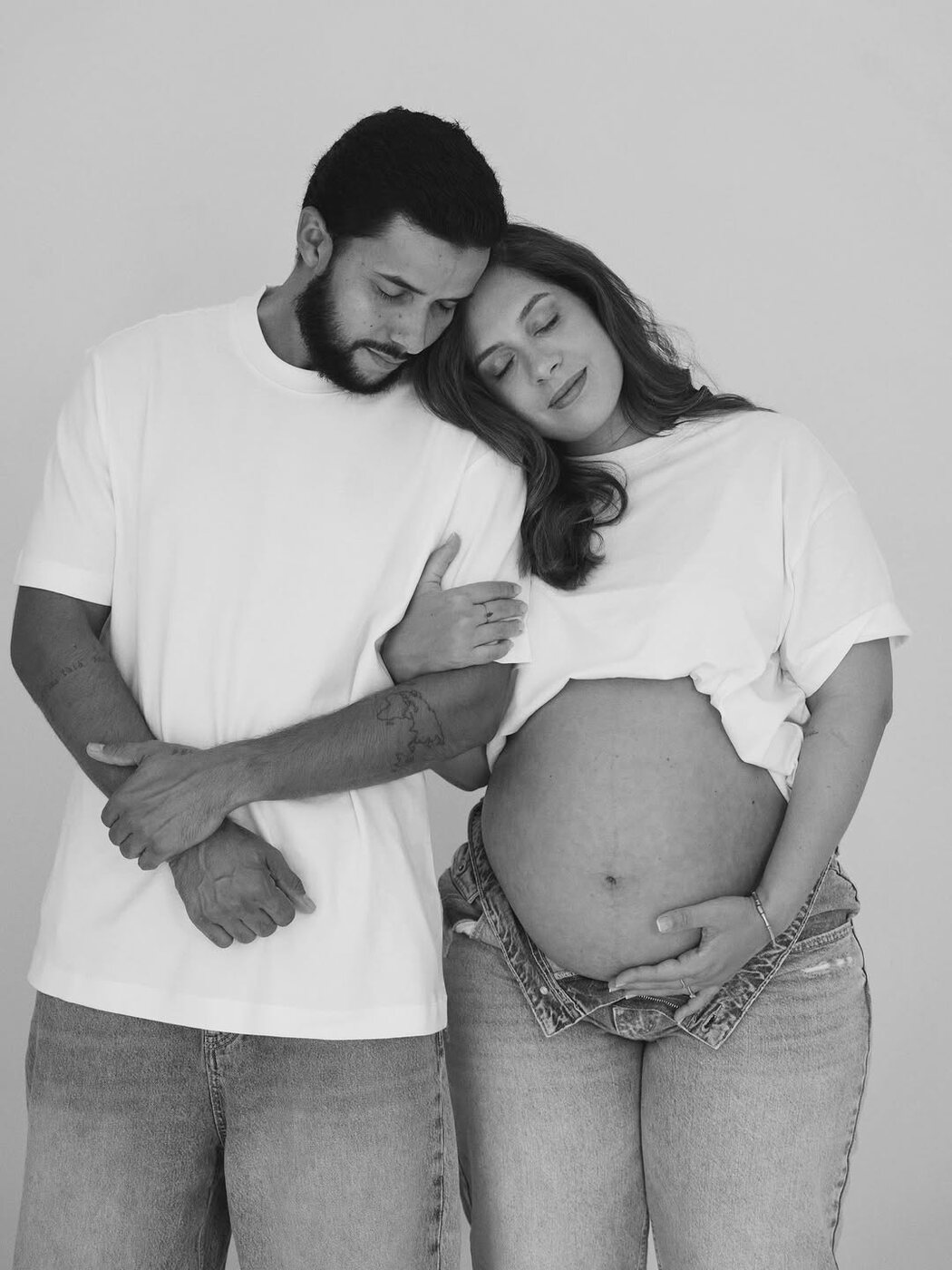 Casal grávido em estúdio, os dois de olhos fechados